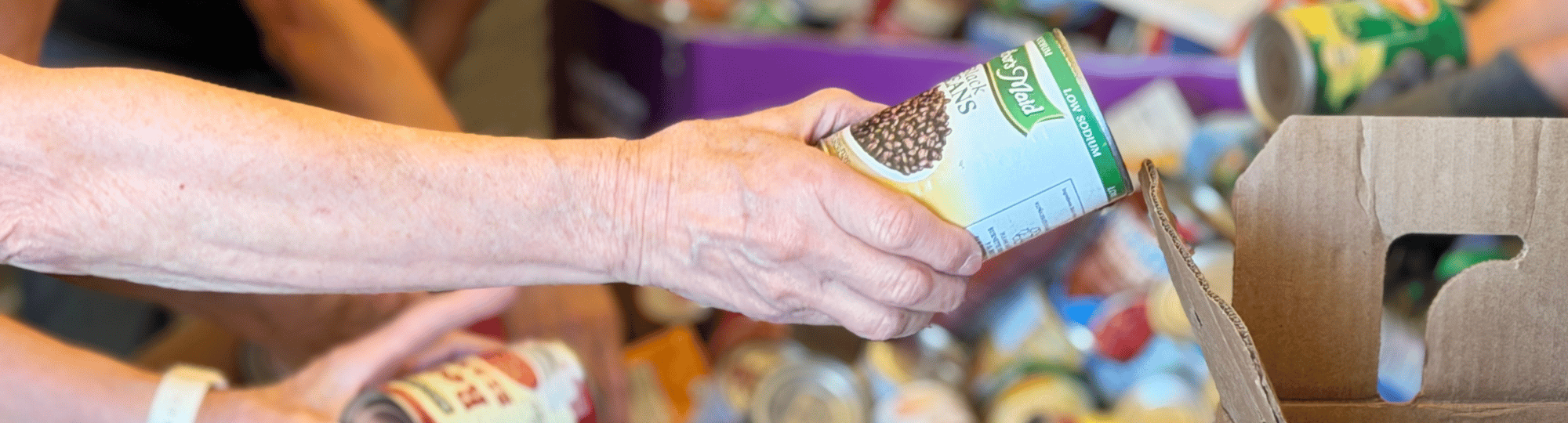 Woman hands can of food to another person packing up food for a local pantry.