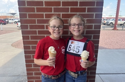 Two girls enjoy ice cream from the Scoops Ice Cream Parlor at the 2024 Nebraska State Fair