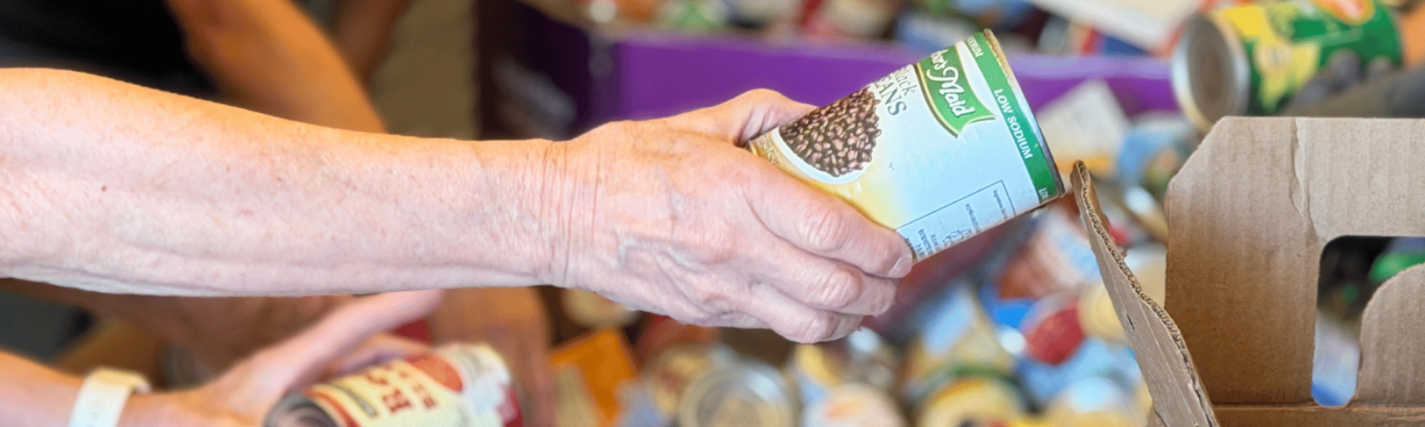 Woman hands can of food to another person packing up food for a local pantry.