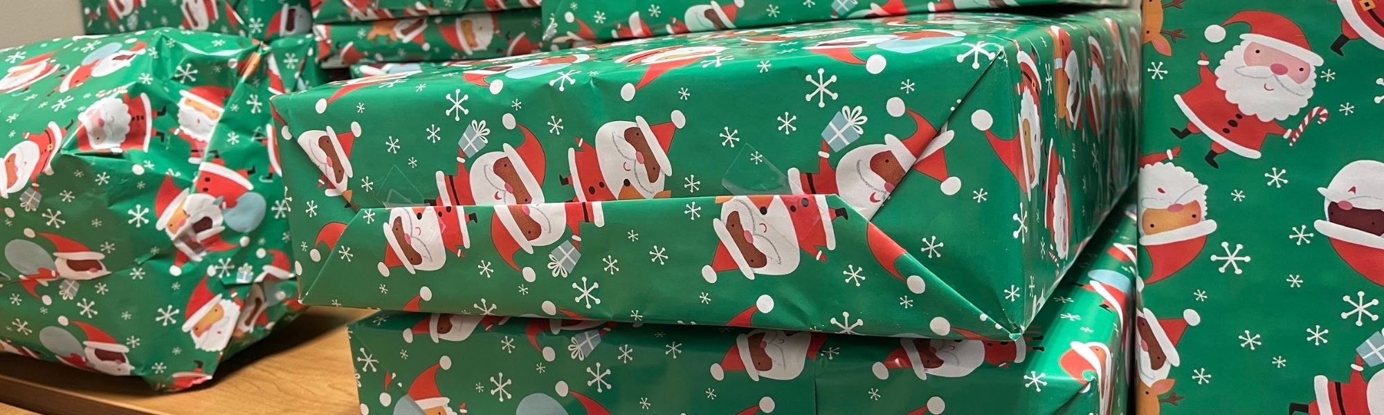 Packages wrapped with green Santa wrapping paper piled on a table.
