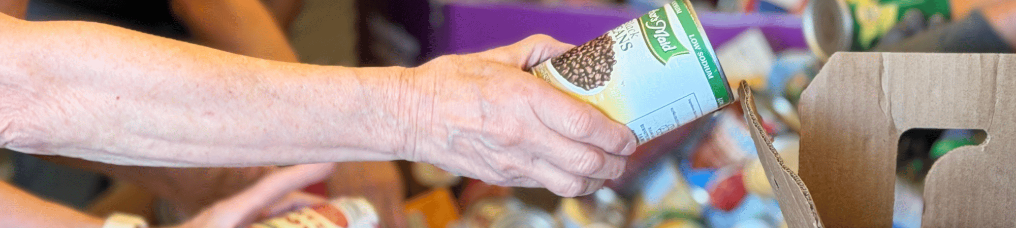 A woman hands a ban of beans to another person filling boxes during Heartland United Way Annual Food Drive in 2026. 