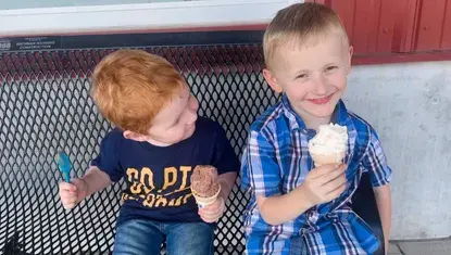 Two boys eat ice cream on a bench in front of Scoops Ice Cream Parlor.